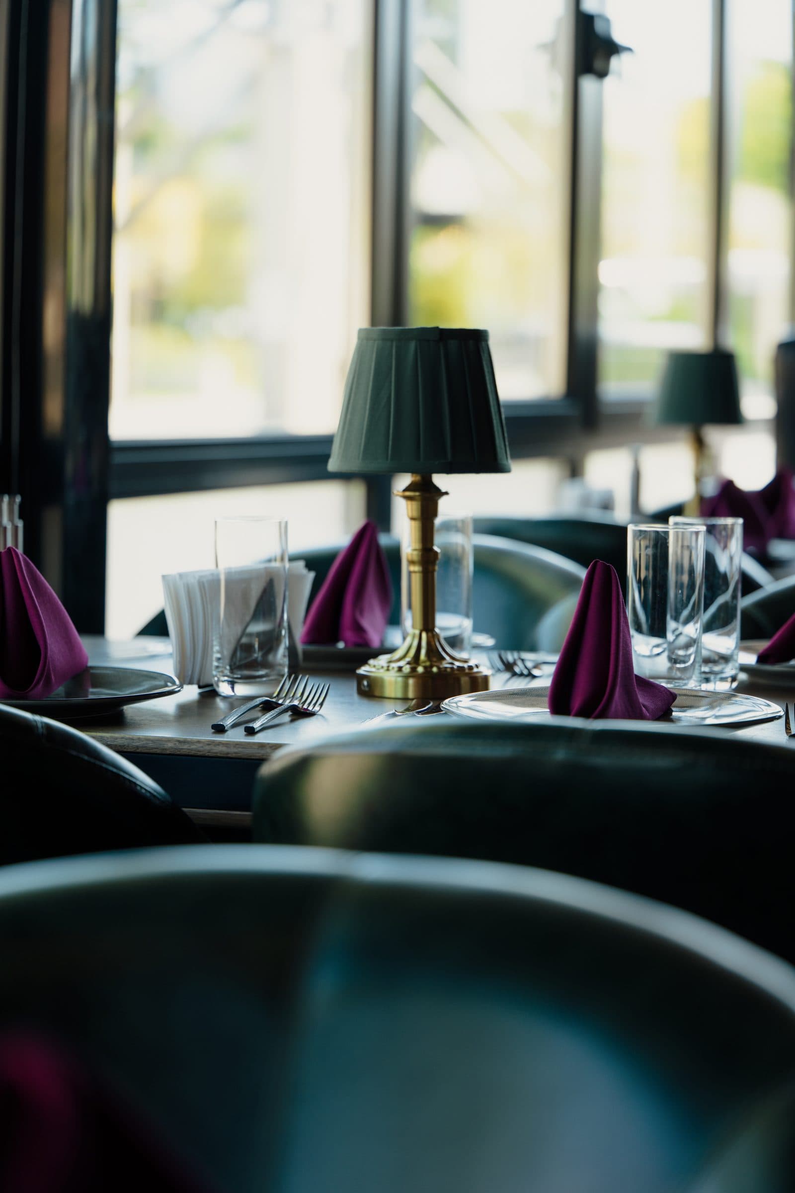 A brass table lamp on a set table by the window