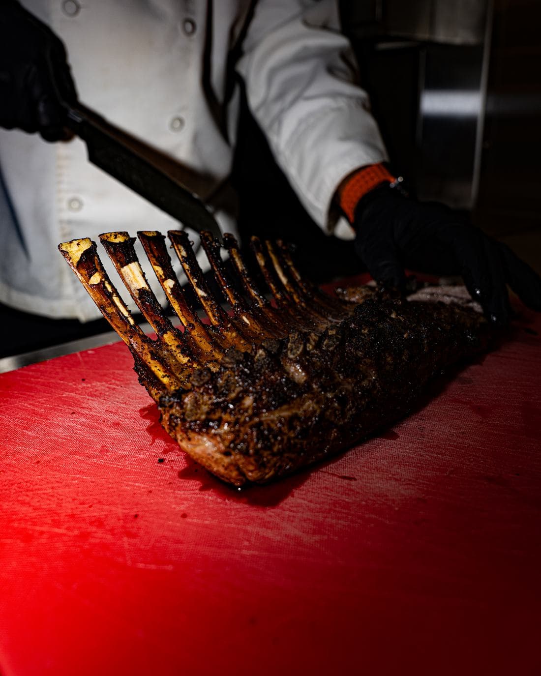 A chef carving a grilled rack on the board